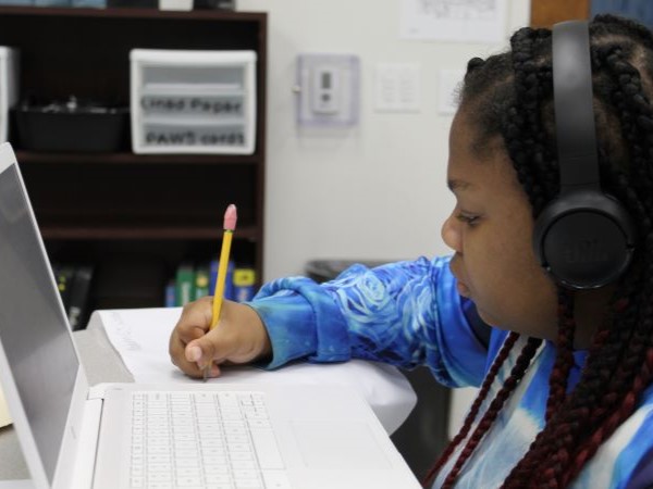 Student wearing headphones sitting at the computer taking notes