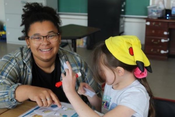 Teacher smiling as student works at her desk