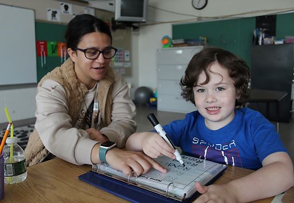 Student smiling as he receives instruction from his teacher