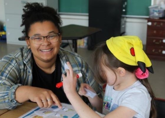 Teacher smiling as student works at her desk