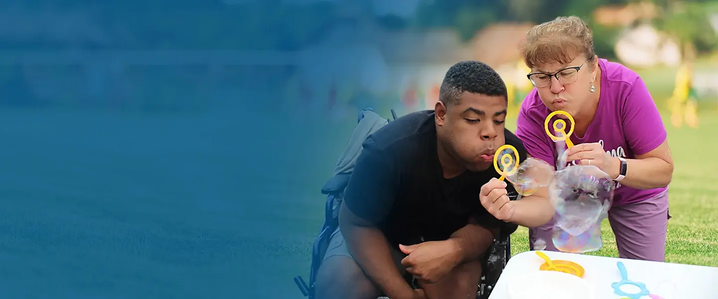 A teacher and student blowing soap bubbles together outdoors during a school activity